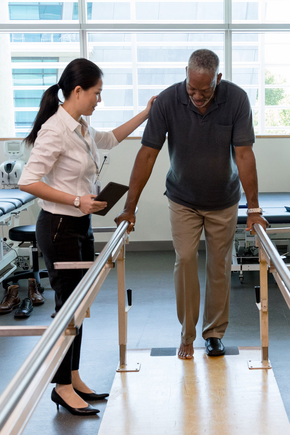 therapist helping senior man do physical therapy on balance bars